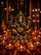 A golden brass Ganesha idol seated on a lotus base, surrounded by lit diya lamps, marigold flowers, and hanging garlands in a warm, festive setting.