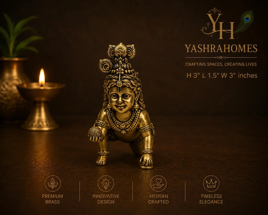 A brass baby figurine of Lord Krishna in a crawling pose, displayed on a dark brown surface with a lit diya and a potted plant in the background. The image features branding for 'Yashrahomes' and feature icons for premium brass, innovative design, artisan craftsmanship, and timeless elegance.