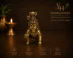 A brass baby figurine of Lord Krishna in a crawling pose, displayed on a dark brown surface with a lit diya and a potted plant in the background. The image features branding for 'Yashrahomes' and feature icons for premium brass, innovative design, artisan craftsmanship, and timeless elegance.