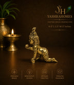 A brass Lord Krishna figurine in a kneeling pose, displayed on a dark brown surface with a lit diya and a gold-toned vase in the background. The image features branding for 'Yashra Homes' and feature icons for premium brass, innovative design, artisan crafted, and timeless elegance.